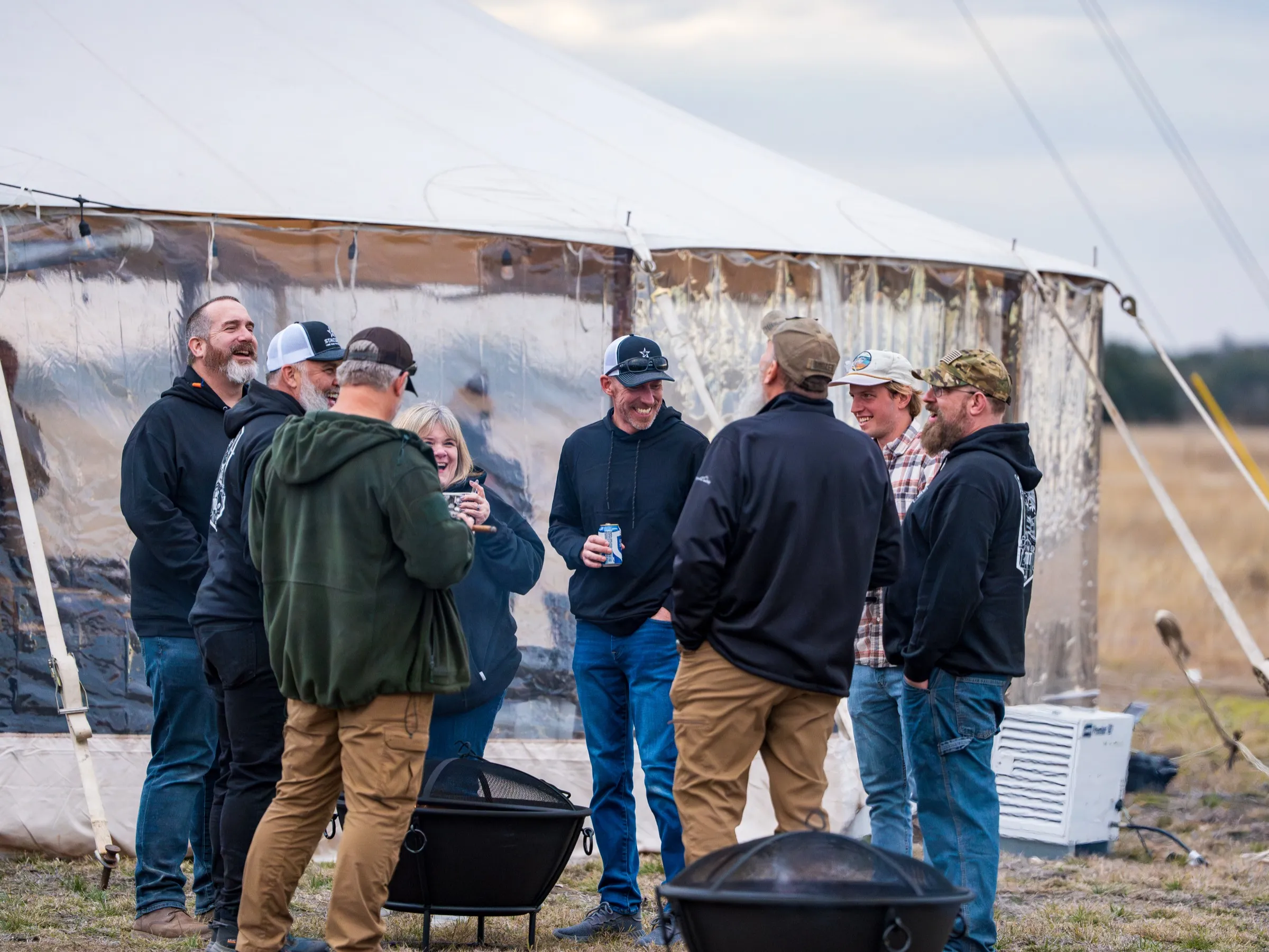 Attendees laughing around fire pits outside the dinner tent at Staccato Ranch