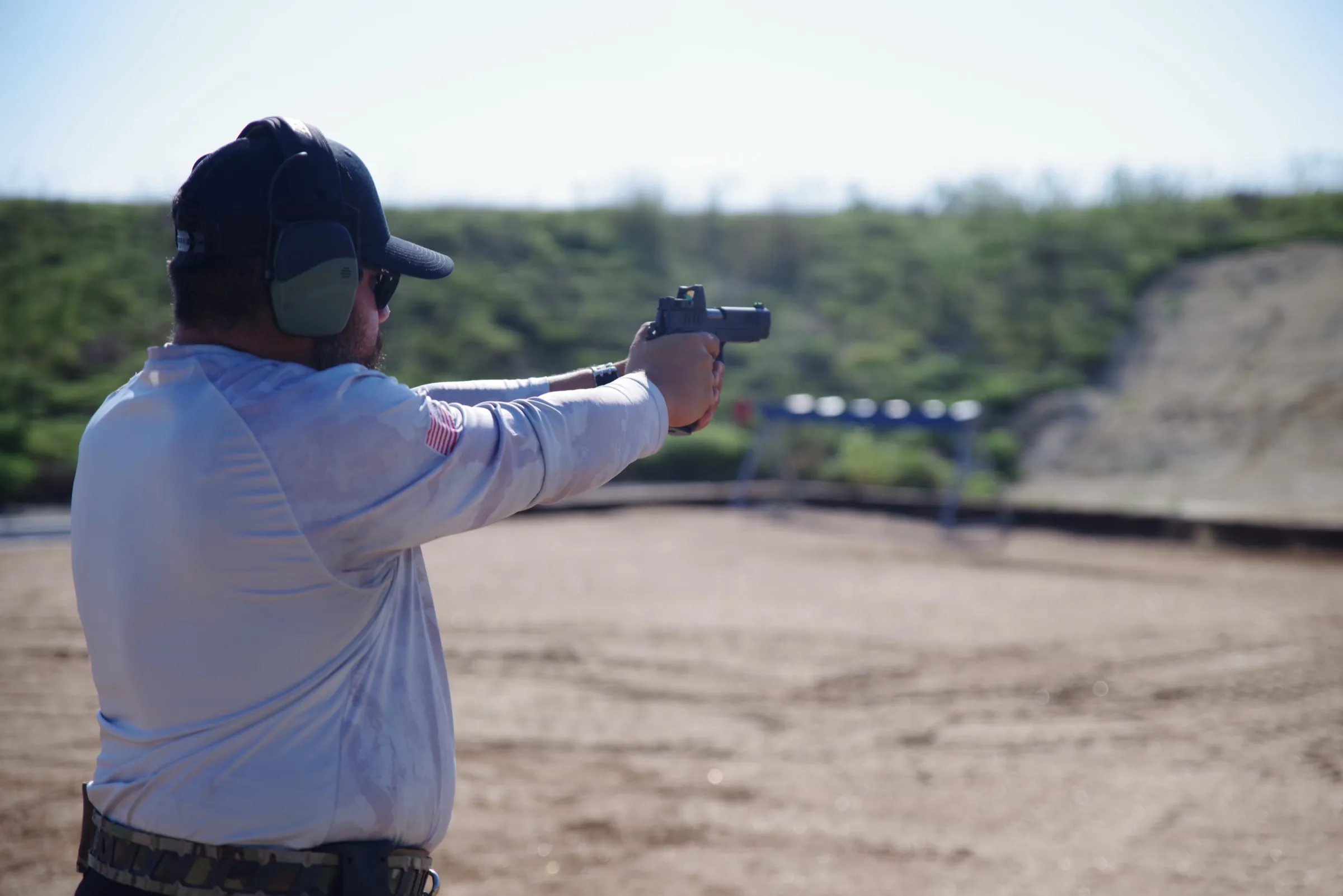 Shooter aiming a red-dot pistol downrange at steel targets in the pistol bay
