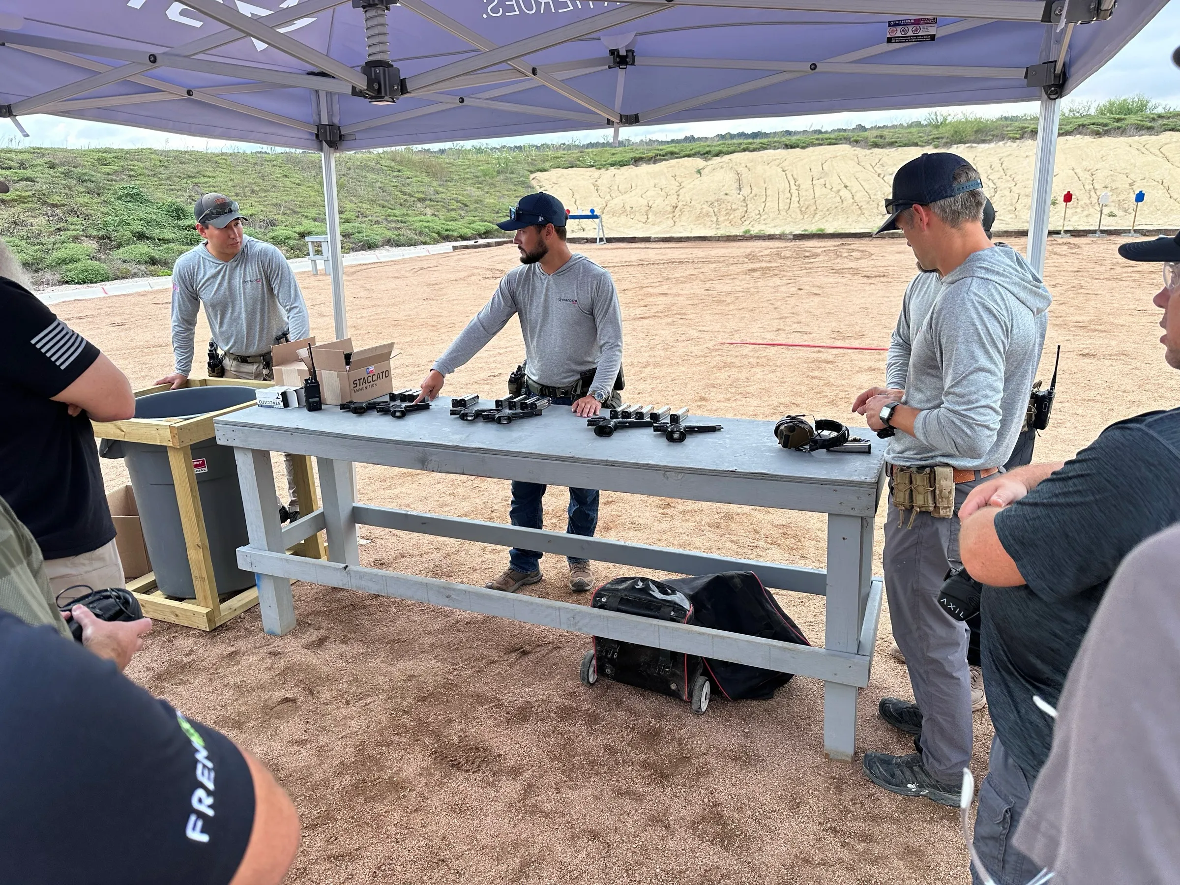 Staccato instructors laying out pistols and optics on a bench under the range tent